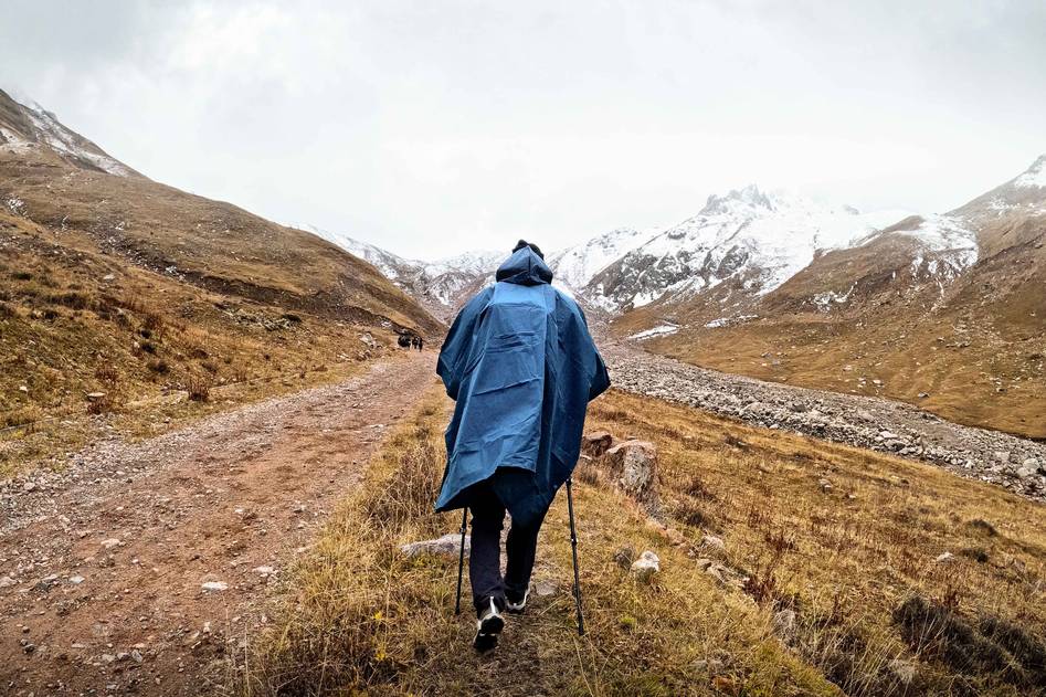 Traveler wearing a stylish waterproof poncho standing on a misty mountain trail with backpack and rolling hills in the background